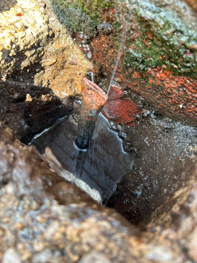Water spraying from a split copper pipe in the ground