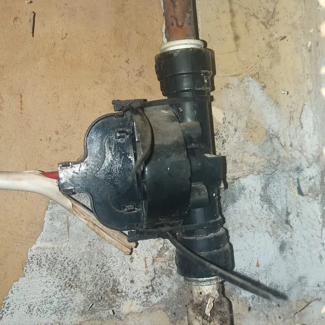 An old black plastic fitting on a water pipe, inside a boxed-in section of wall