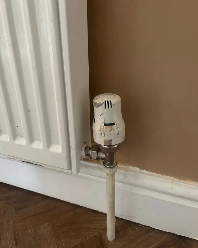A white thermostatic radiator valve on a panel radiator, above a wooden floor