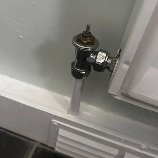 A chrome radiator valve with its thermostatic head taken off, beside a white radiator