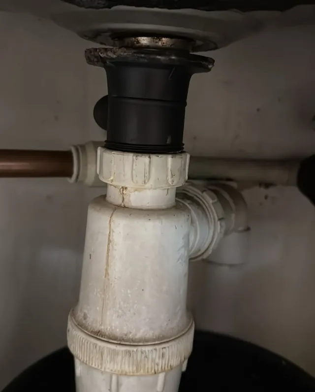 A white bottle trap and waste fitting on the underside of a kitchen sink