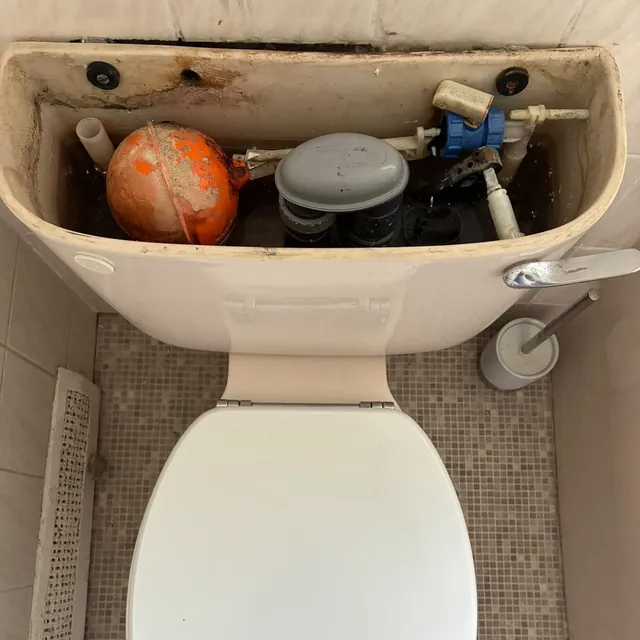 The inside of an older toilet cistern with a worn ball valve and an orange float